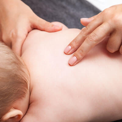 A chiropractor gently pressing on an infant's back with two fingers.