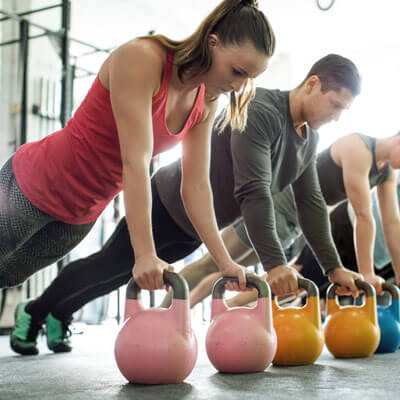 man and woman doing kettle bell planks in a gym