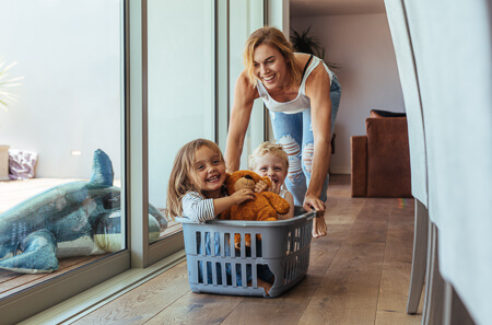 Mom pushing her young kids in a laundry basket