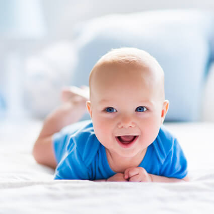 Little baby in blue onesie doing tummy time on bed
