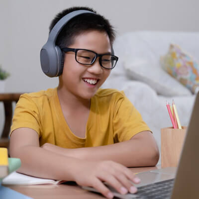 boy in yellow shirt with headhphones playing on computer