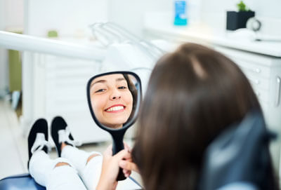 girl looking in mirror smiling at dental office