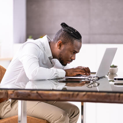 Man hunched typing on small computer