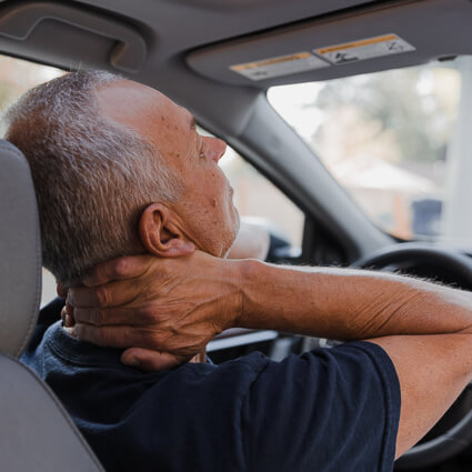 person holding their neck while sitting at a steering wheel