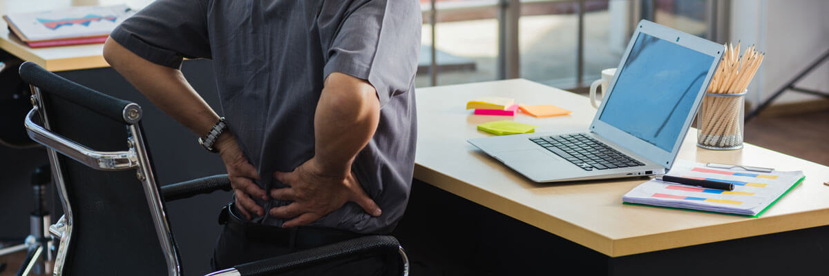 Man in an office chair holding his lower back in pain