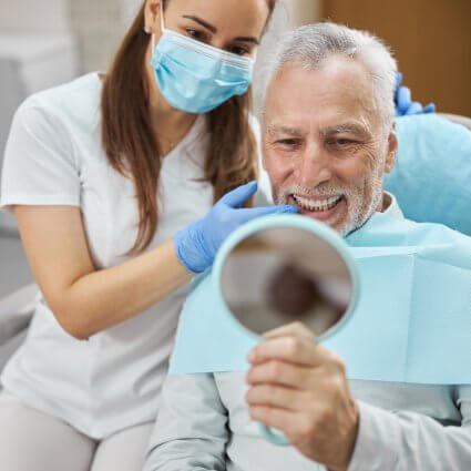 man smiling in mirror with dental hygienist