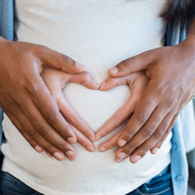 A pregnant woman and her partner holding their hands in the shape of a heart over her belly