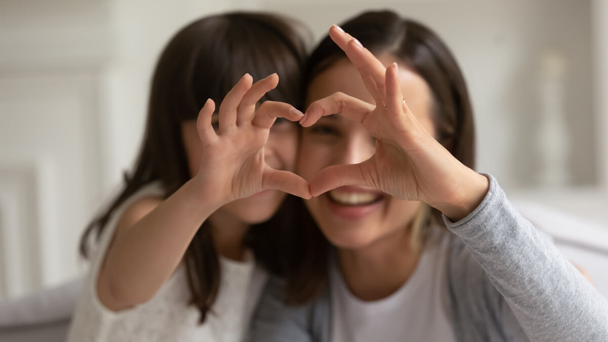 Mother and daughter forming the shape of a heart with their hands