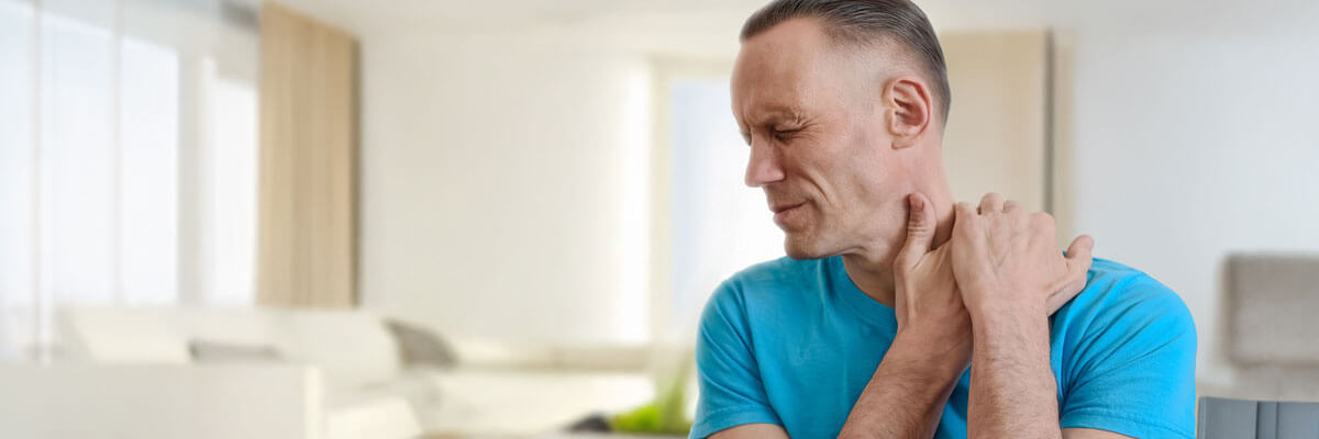 older man indoors with neck pain holding neck and turning head sideways