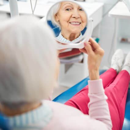 Older woman in dental chair smiling in mirror