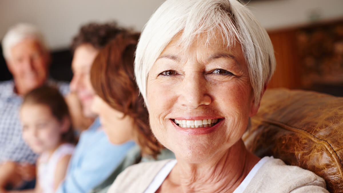 older woman siting on couch smiling with beautiful teeth