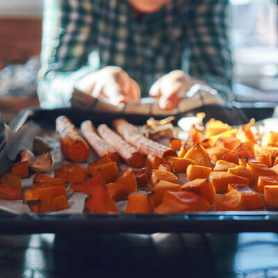 person putting tray of veggies into oven