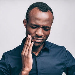 Man in blue shirt holding hand to jaw