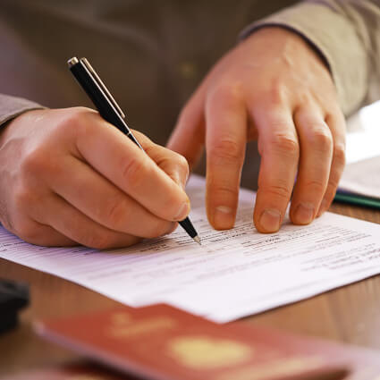 Person filling out paperwork with pen on desk