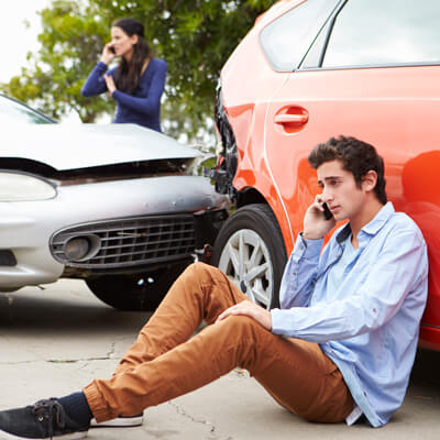 Man sitting next to car on phone after accident