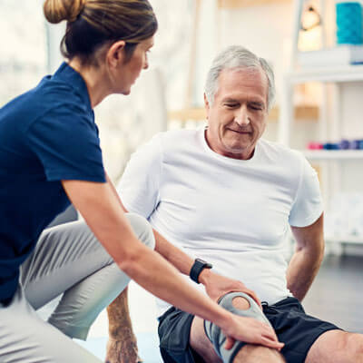 Physical therapist and older man with brace on knee