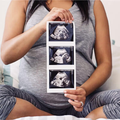 Pregnant woman holding sonagrams to the camera