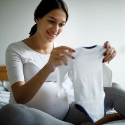 Pregnant woman holding up baby clothes