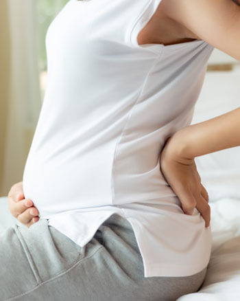 woman sitting on bed holding back and baby bump