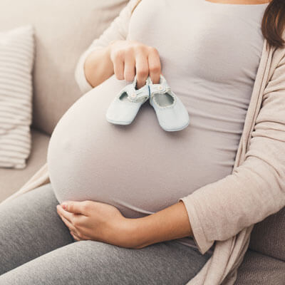 closeup of pregnant woman sitting on couch with baby shoes on belly