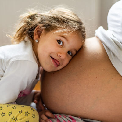 Litte girl with head on moms pregnant belly