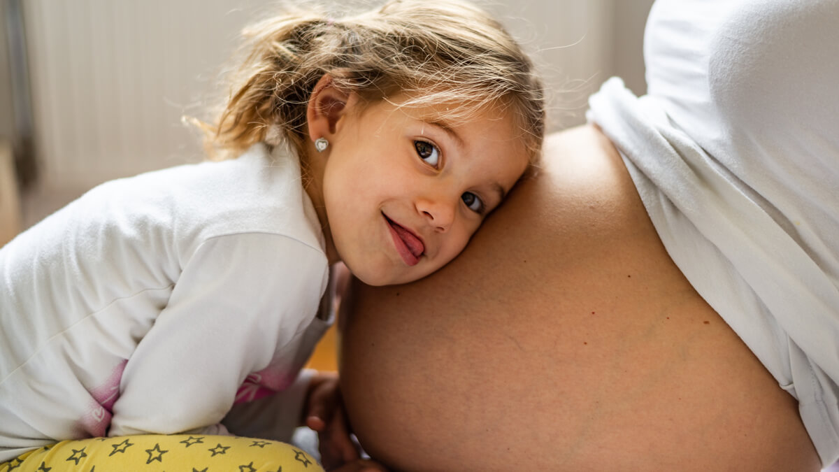 Cute girl with head on mom's pregnant belly