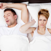 Man snoring and woman with pillow over her ears