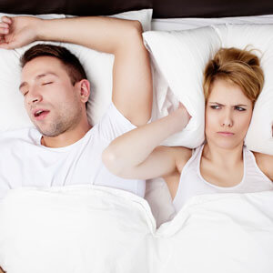 Woman with pillow over her ears, next to snoring partner in bed