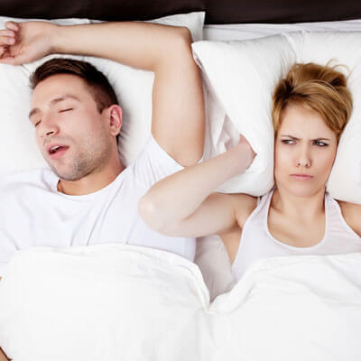 woman awake covering ears next to man snoring