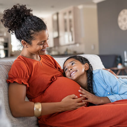 pregnant woman and daughter smiling down at her stomach
