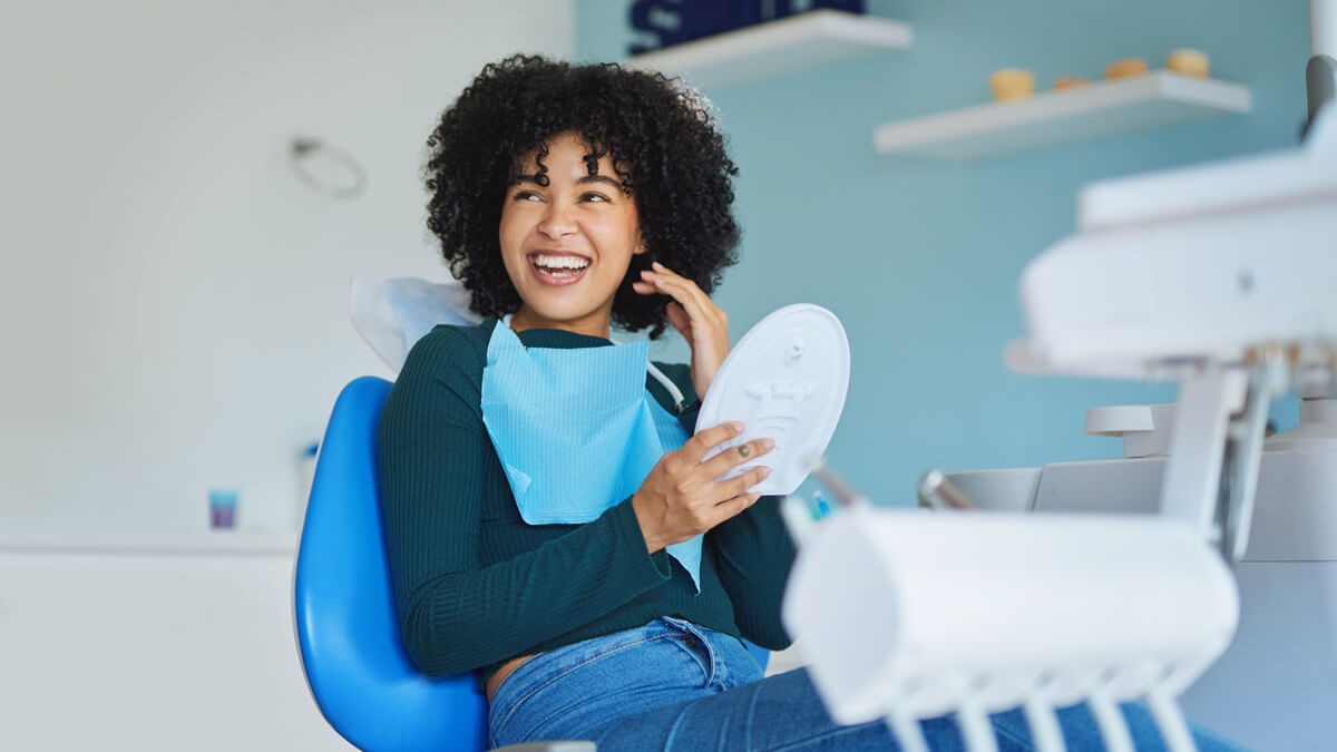 Woman with a mirror smiling gratefully at the dentist