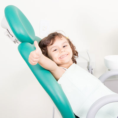 Little girl in dentist chair giving thumbs up