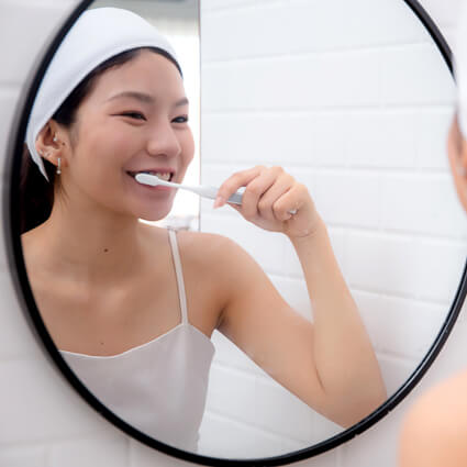 woman looking in mirror brushing her teeth