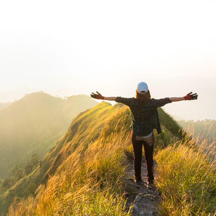 Woman atop grassy hill with arms outstretched