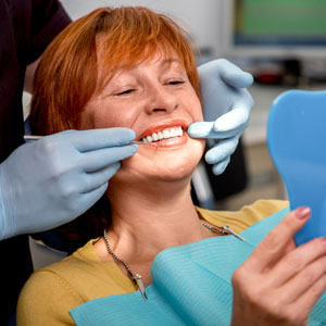 Woman admiring smile in mirror in dentist chair