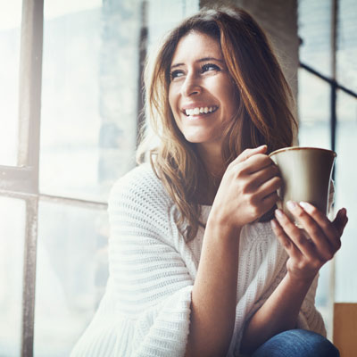 Woman with long brown hair sitting near window with coffee mug