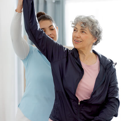 woman in black zipup raising arm with practitioner helping