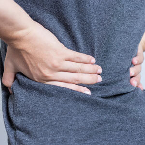 Woman in gray shirt holding body in pain