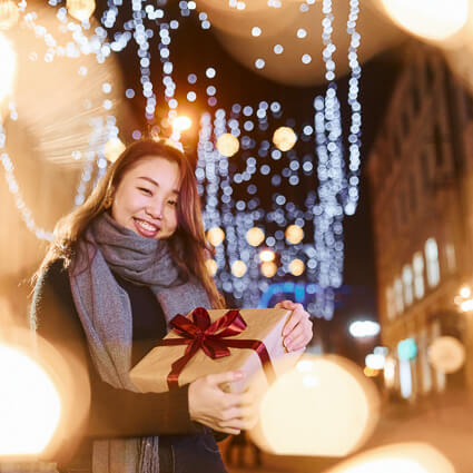 Woman outdoors holding present among glowing lights