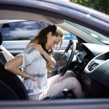 woman sitting in the car holding shoulder and back