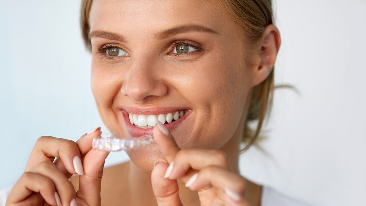 Woman smiling as she holds her clear aligners