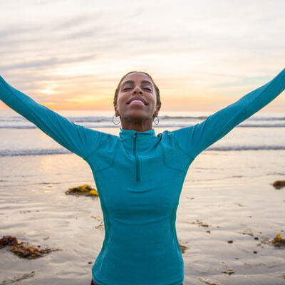 smiling person with arms outstretched at beach