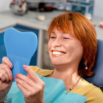 Woman with red hair in dentist chair admiring her smile in a mirror