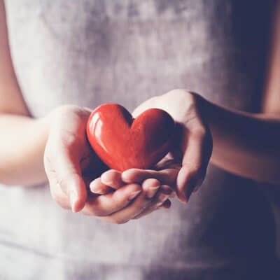 closeup of hands holding wooden red heart