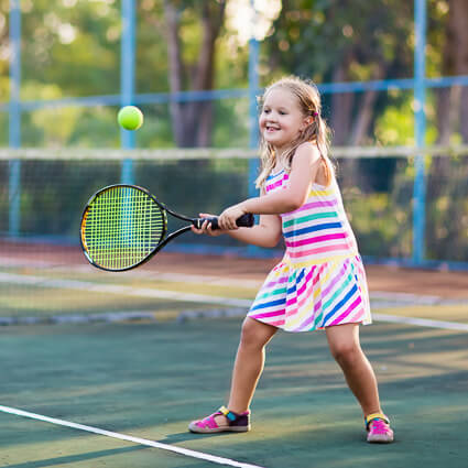 Young girl in rainbow dress hitting tennis ball