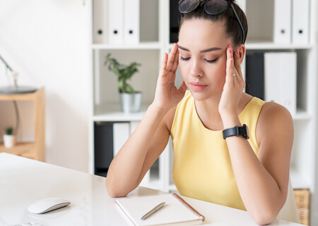 woman sitting at a desk with a migraine